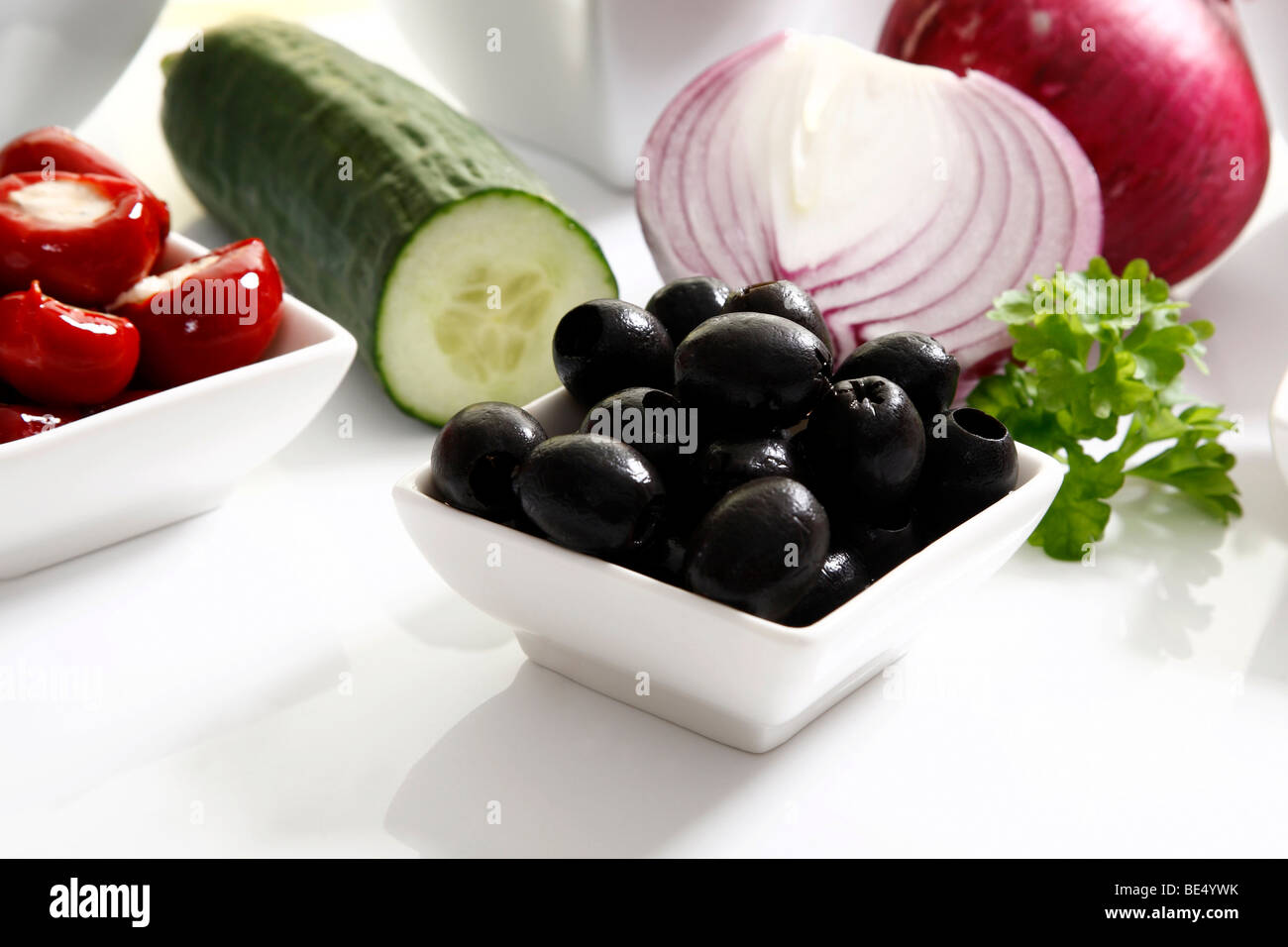 Schwarze Oliven in einer kleinen Schüssel neben Zwiebeln, Gurken und Paprika Stockfoto