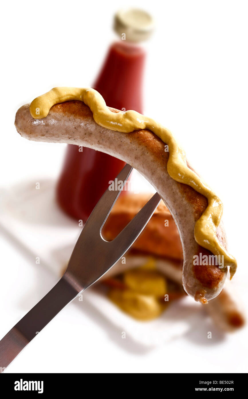 Roll-Bratwurst Wurst mit Senf auf einer Grill-Gabel vor Ketchup und ein Brot Stockfoto