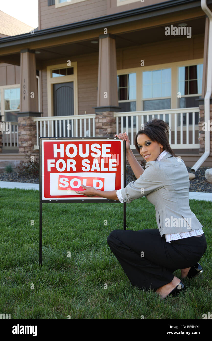 Weibliche Grundstücksmakler Zeichen vor Haus verkauft aufsetzen Stockfoto