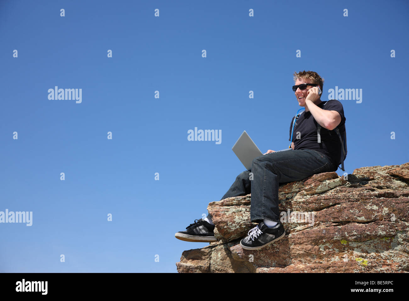 Junger Mann mit Laptop und Handy auf Klippe Stockfoto