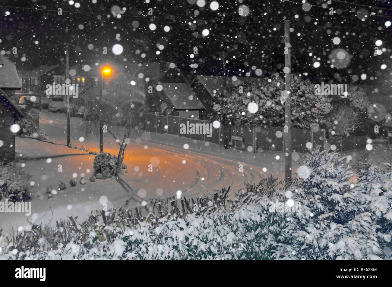 Nachtschneeflocken Kamera Blitz orange Lampenpfosten Licht auf schneebedeckte Straße in Wohnlandschaft manipuliert hauptsächlich schwarz-weiß England Großbritannien Stockfoto