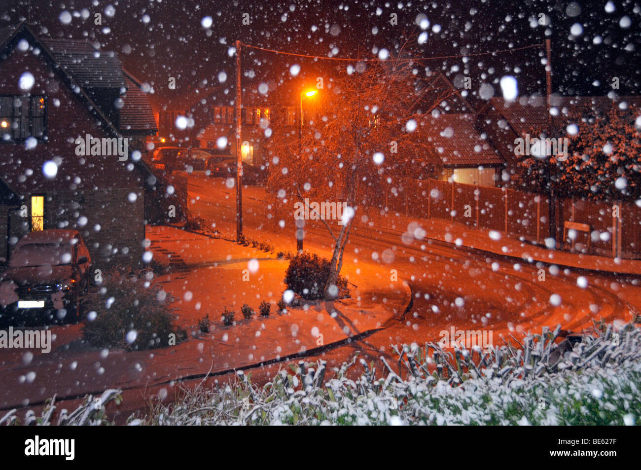 Schneeflocken durch Blitz mit orangefarbener Natriumbeleuchtung beleuchtet schneebedeckte Nacht Wohnstraße Landschaft Brentwood Essex England Großbritannien Stockfoto