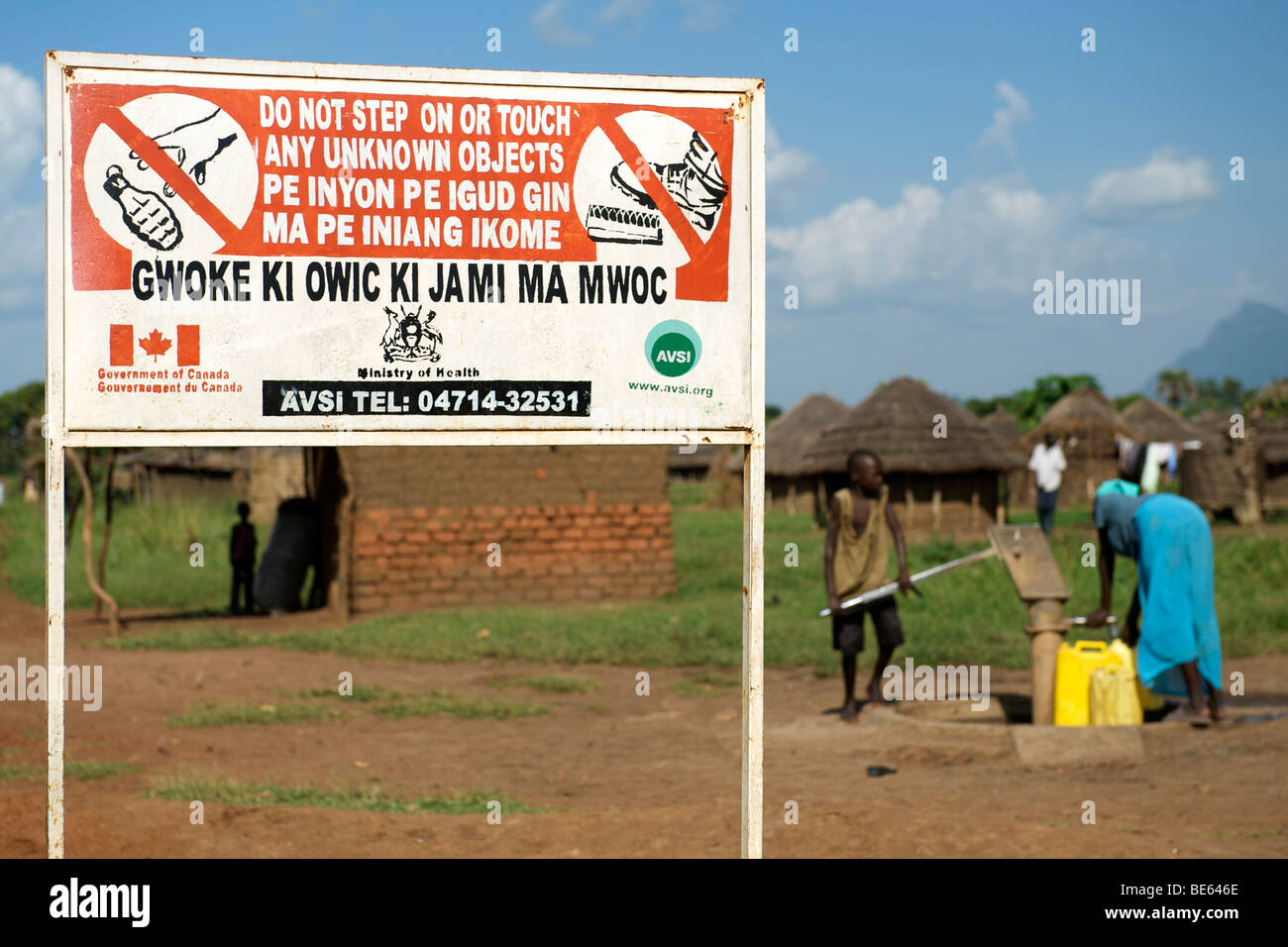 Dorfbewohner, die Wasserpumpen vor ein Schild Warnung von Blindgängern in einem Dorf in Nord-Uganda Kitgum und Umgebung. Stockfoto