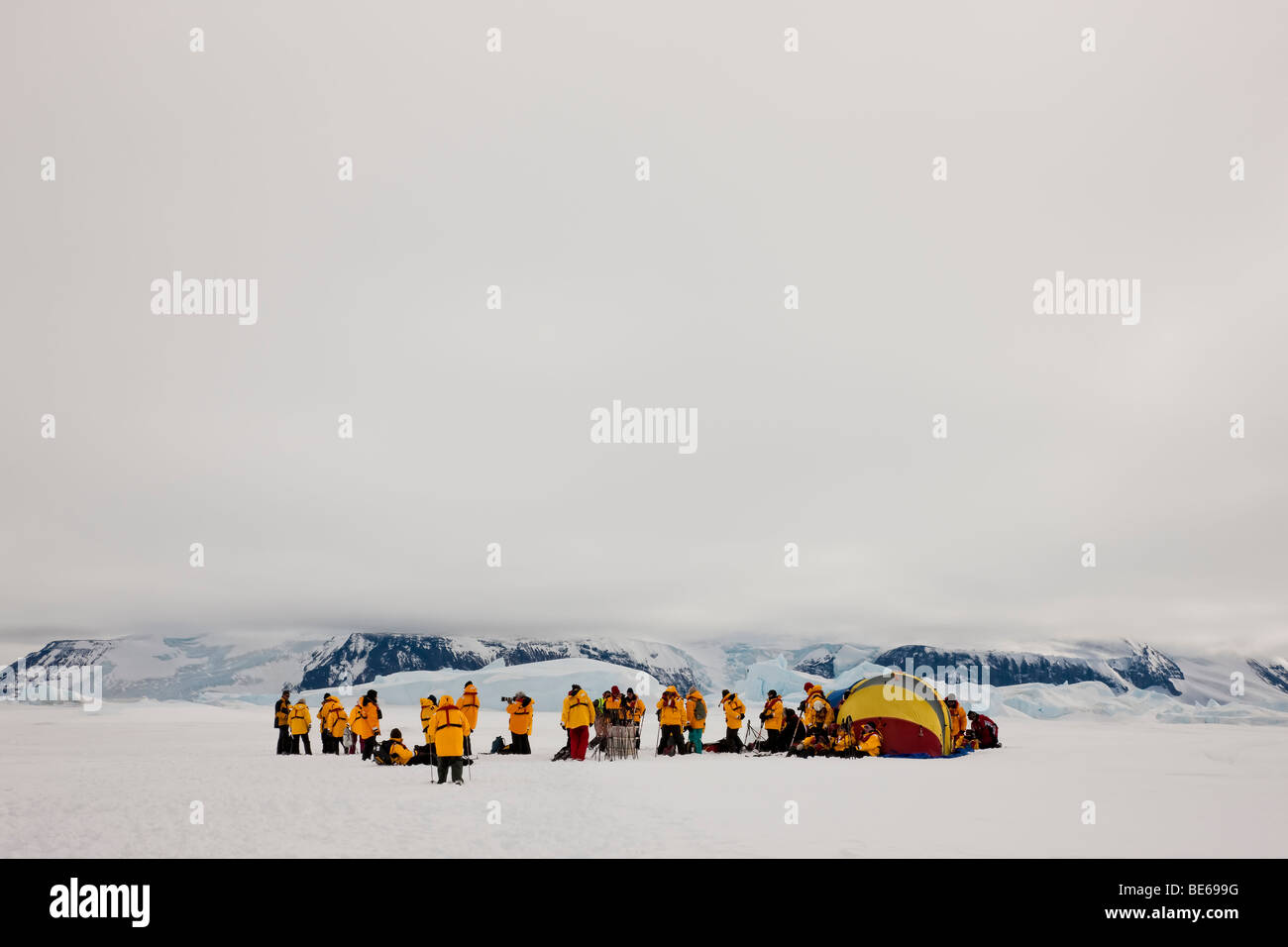 Gruppe der Antarktis eco Touristen sammeln auf Schnee Gap in der Nähe von Schnee bedeckte Berge Gletscher tragen leuchtend gelben Parkas und Gelb survuval Zelt Stockfoto