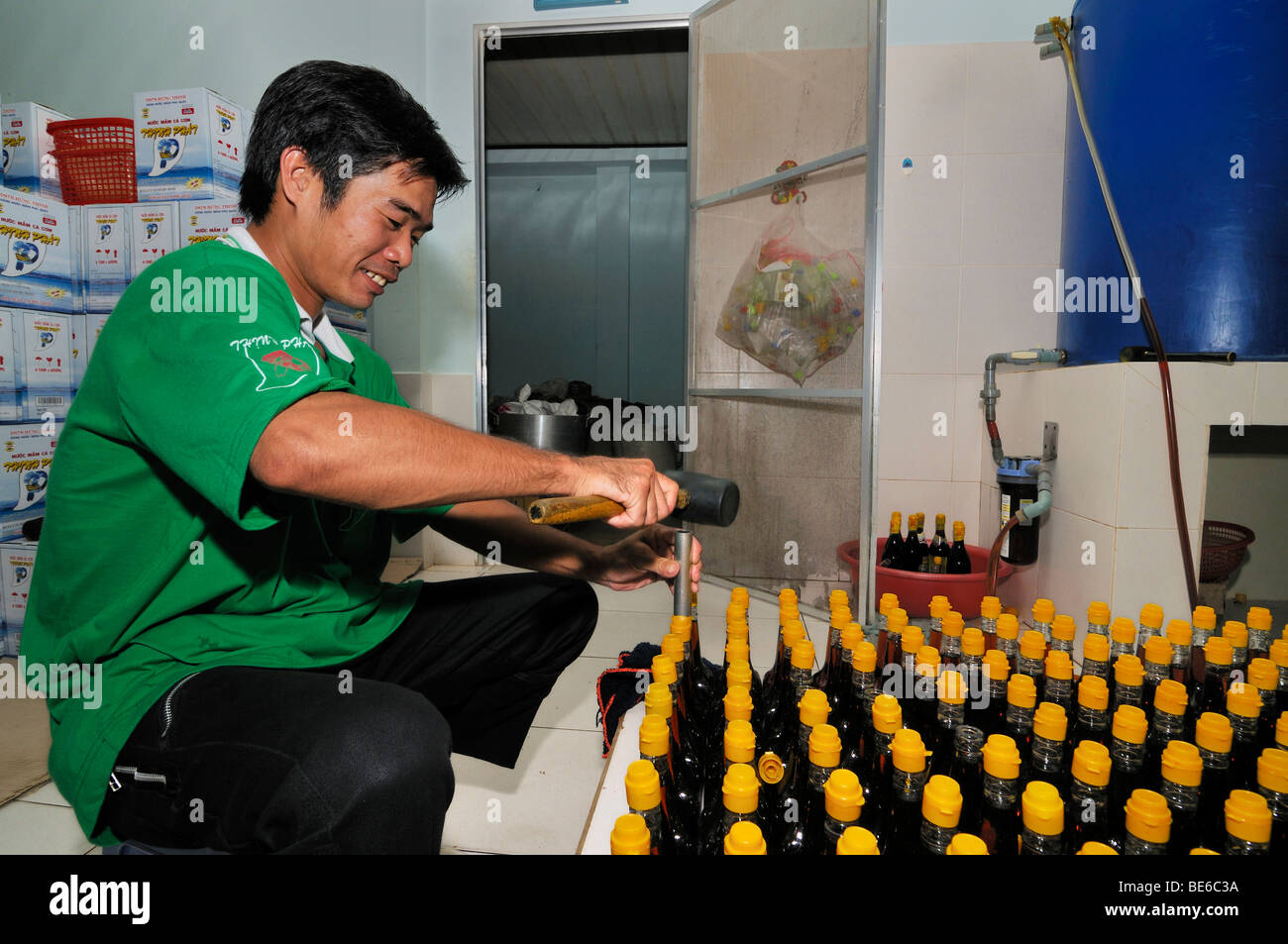 Vietnamesische Mann, der gelbe Kunststoffkappen auf Glasflaschen von der traditionellen vietnamesischen Fisch sauce Nuoc Mam, Phu Quoc, Vietnam Stockfoto