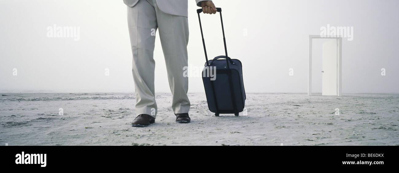Mann zu Fuß mit Rollgepäck am Strand, offene Tür im Abstand Stockfoto