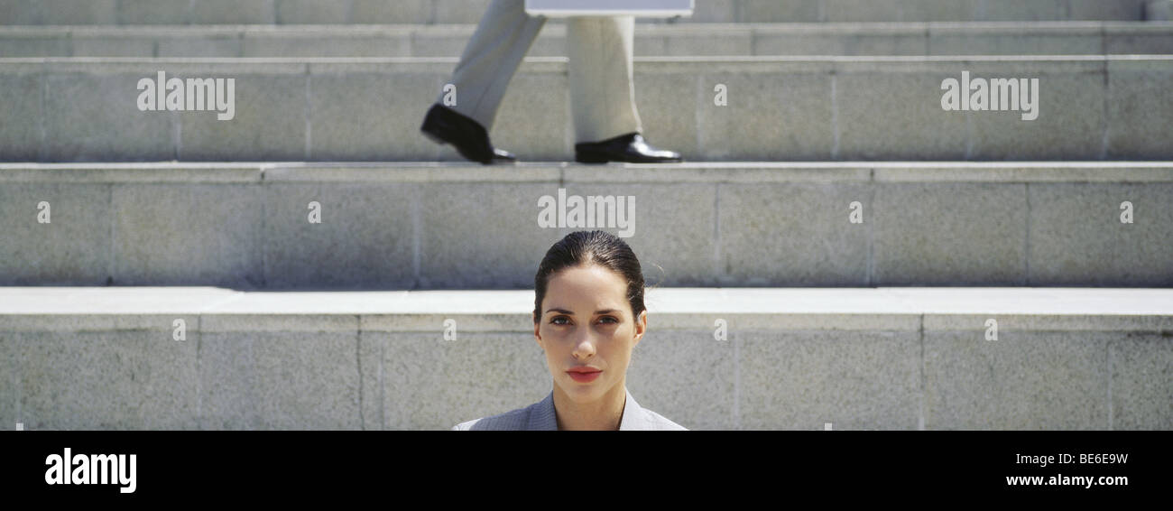 Geschäftsfrau auf Treppe, Blick in die Kamera, Mann im Hintergrund Stockfoto
