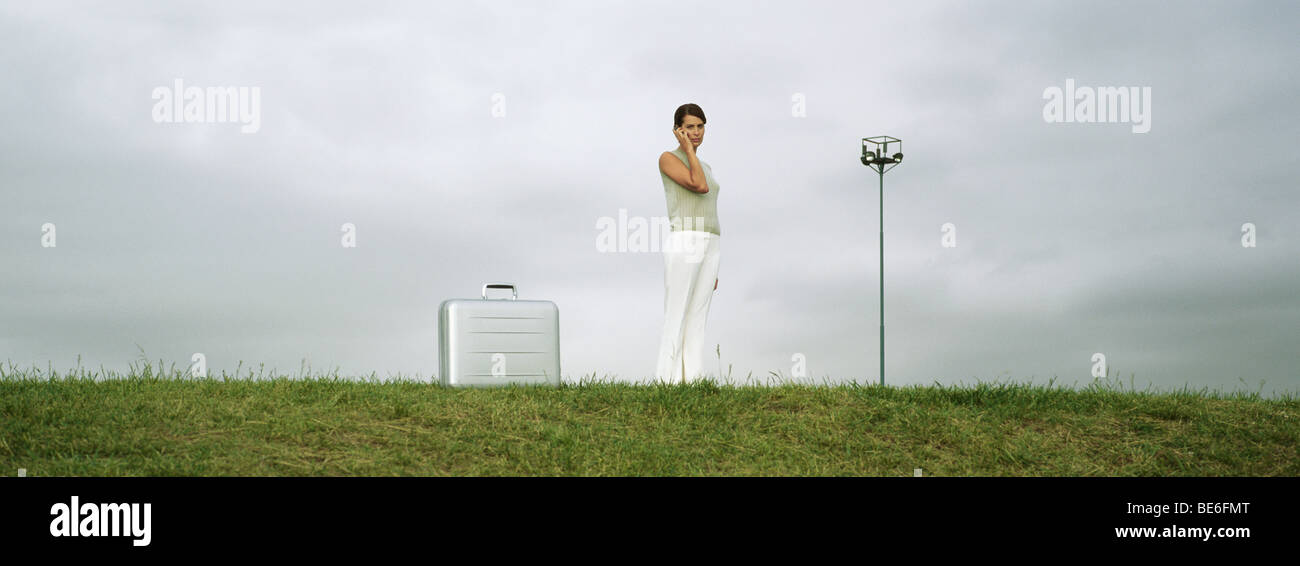 Frau im Feld mit Handy, Aktenkoffer auf Boden in der Nähe Stockfoto