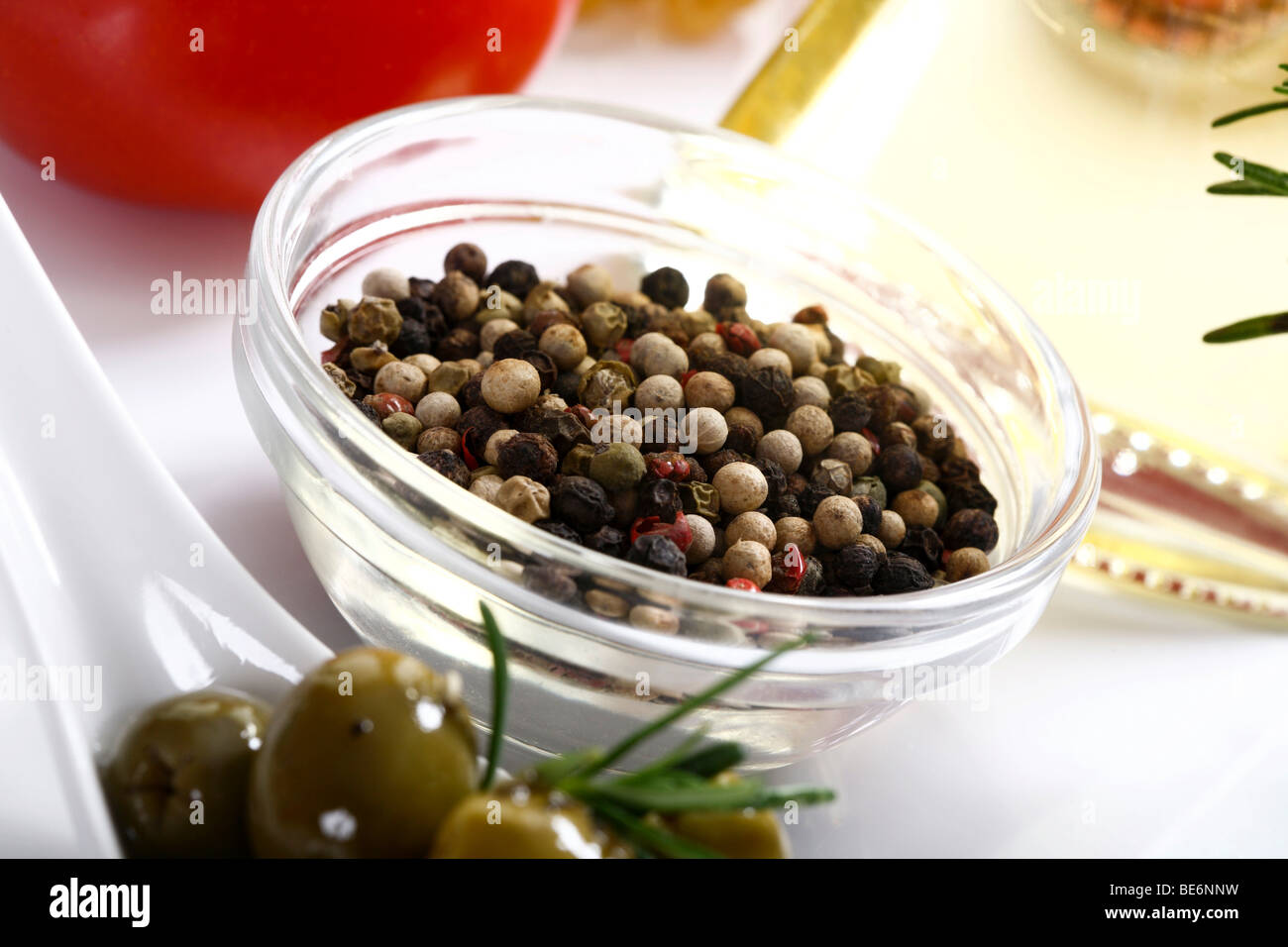 Bunte Pfefferkörner in einer Schüssel neben Olivenöl und Oliven Stockfoto