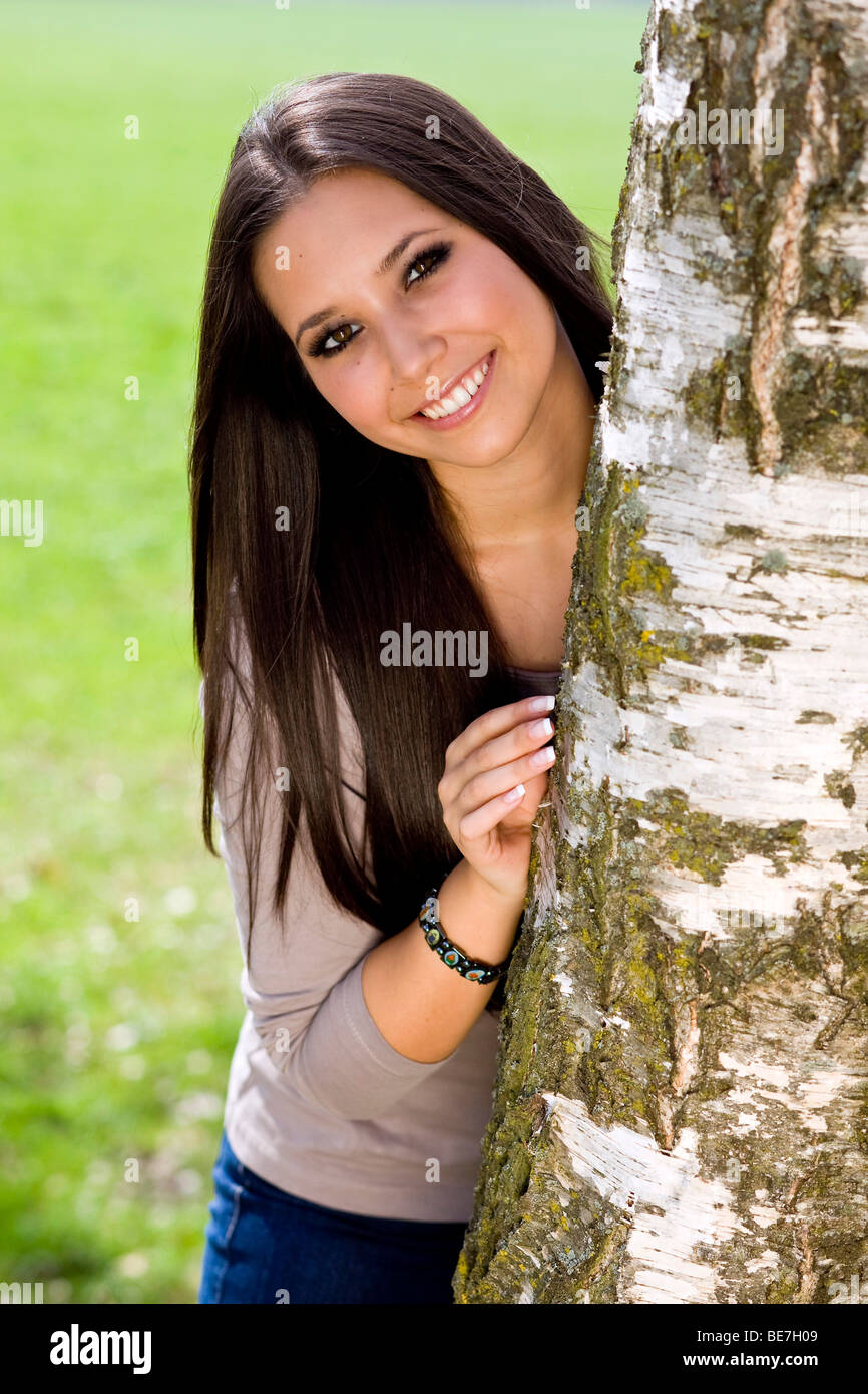 Junge Frau, 20, peering hinter einem Baum Stockfoto