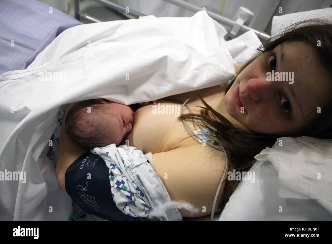 Eine junge Mutter in einem Krankenhaus Kleid stillen ihr neugeborenes Baby Boy zum ersten Mal Stockfoto