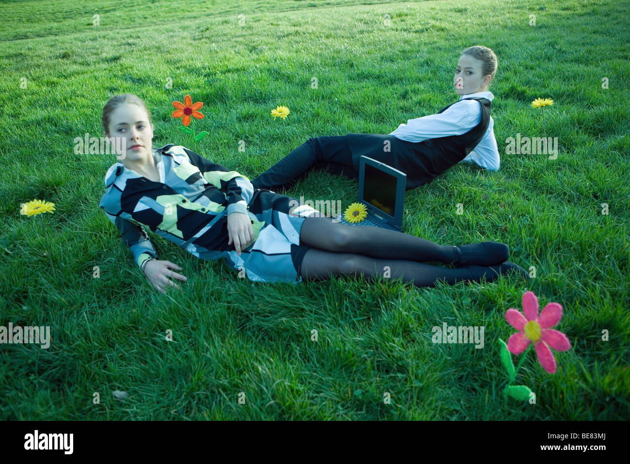 Zwei Frauen in Wiese mit Laptop-Computer zwischen ihnen liegen, schaut man über die Schulter in die Kamera Stockfoto