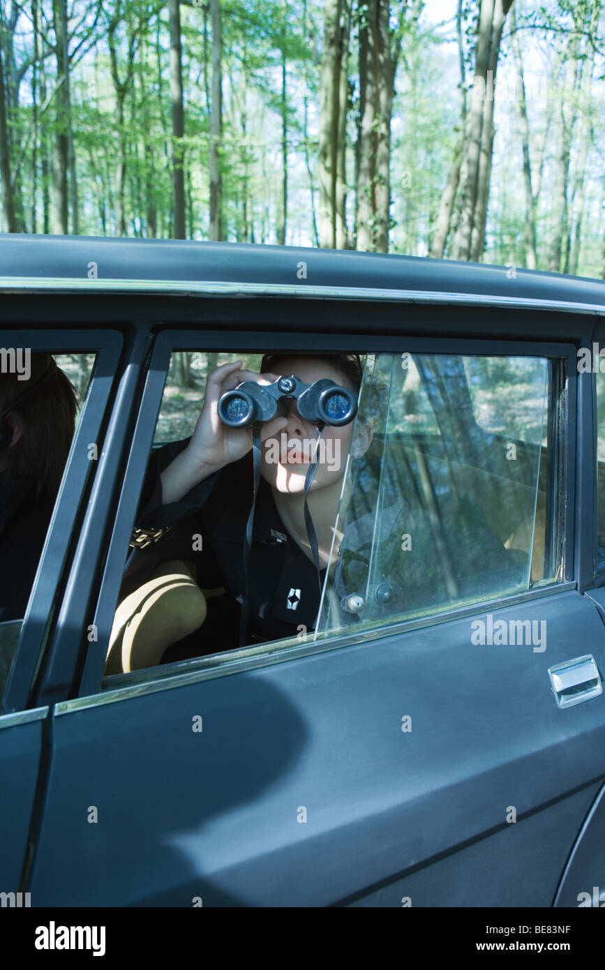 Frau sitzt im Auto, Fenster mit Blick durch ein Fernglas Stockfoto