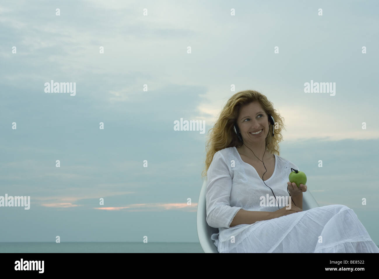 Frau im Freien sitzen, hören Sie Kopfhörer eingesteckt in Apfel, Lächeln Stockfoto