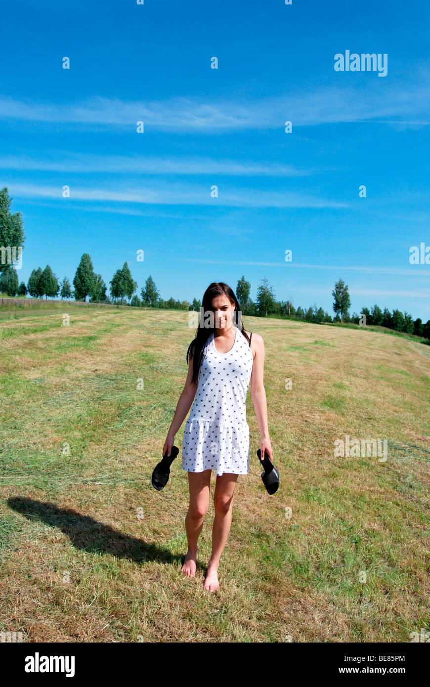 Frau in der Hand durch eine gemähte Wiese mit ihren Schuhen barfuß laufen Stockfoto