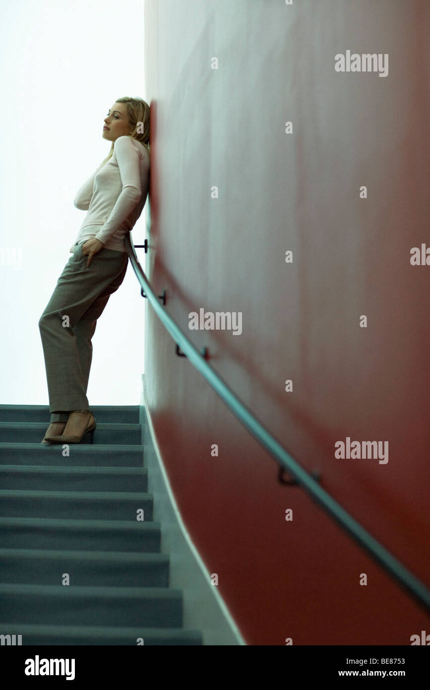 Frau stehend auf der Treppe, Wand gelehnt, wegschauen Stockfoto