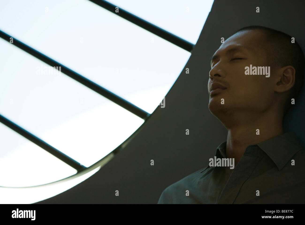 Mann mit geschlossenen Augen in stille Kontemplation durch Fenster mit Balken Stockfoto