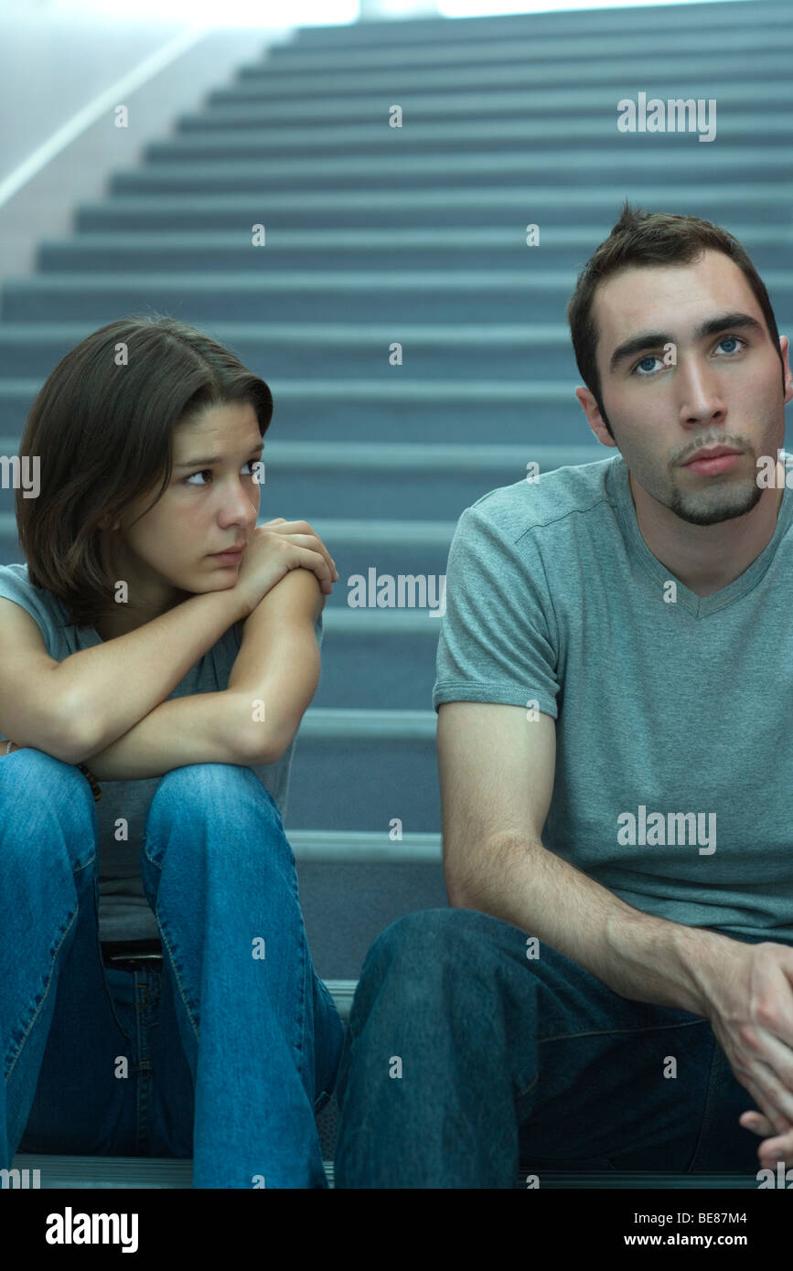 Junges Paar sitzen nebeneinander auf Treppen, Mann wegsehen, Frau beobachten mit Sorge Stockfoto