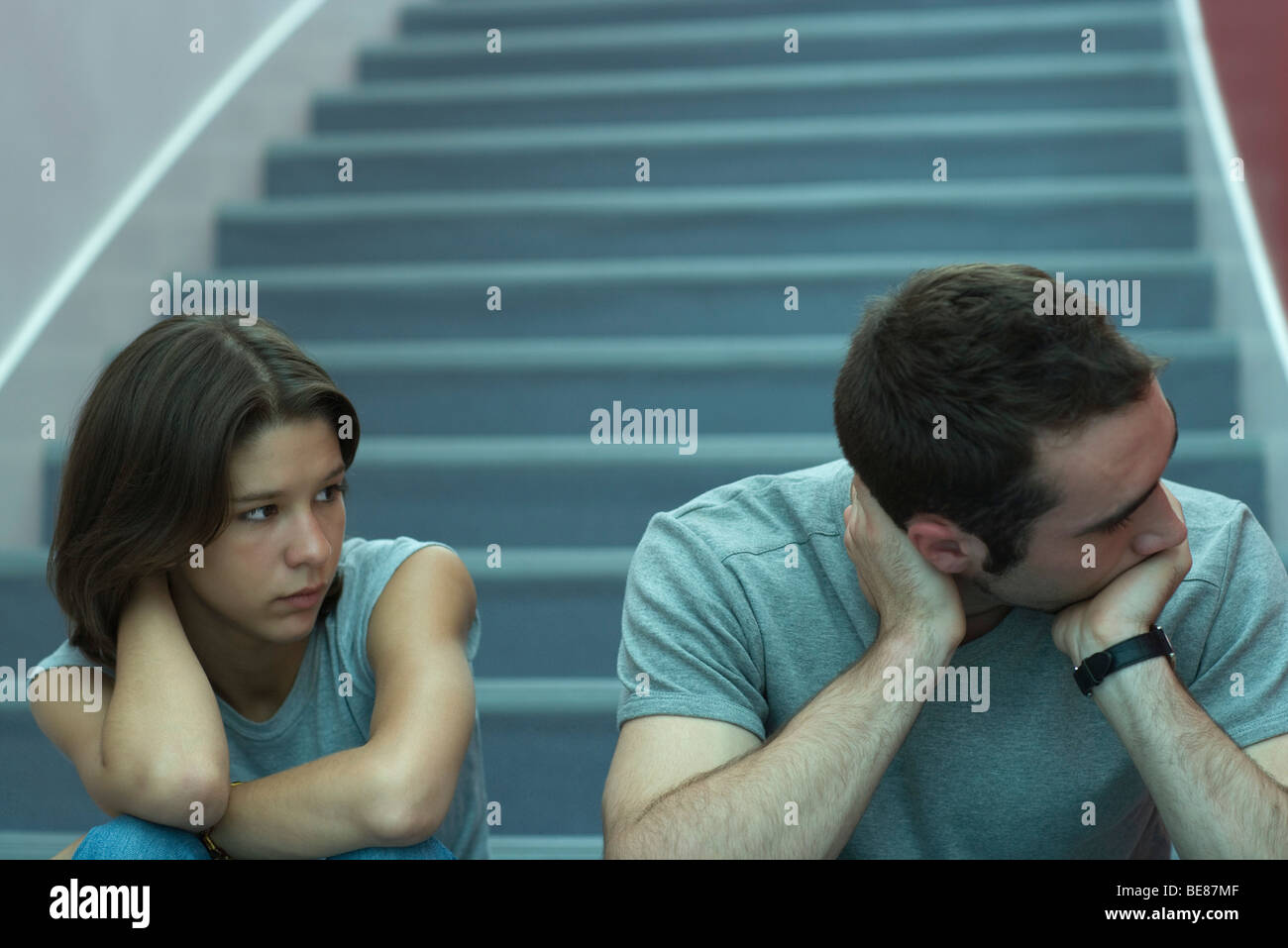 Junges Paar sitzt auf der Treppe, Mann hält Kopf und wegsehen, Frau beobachten Stockfoto