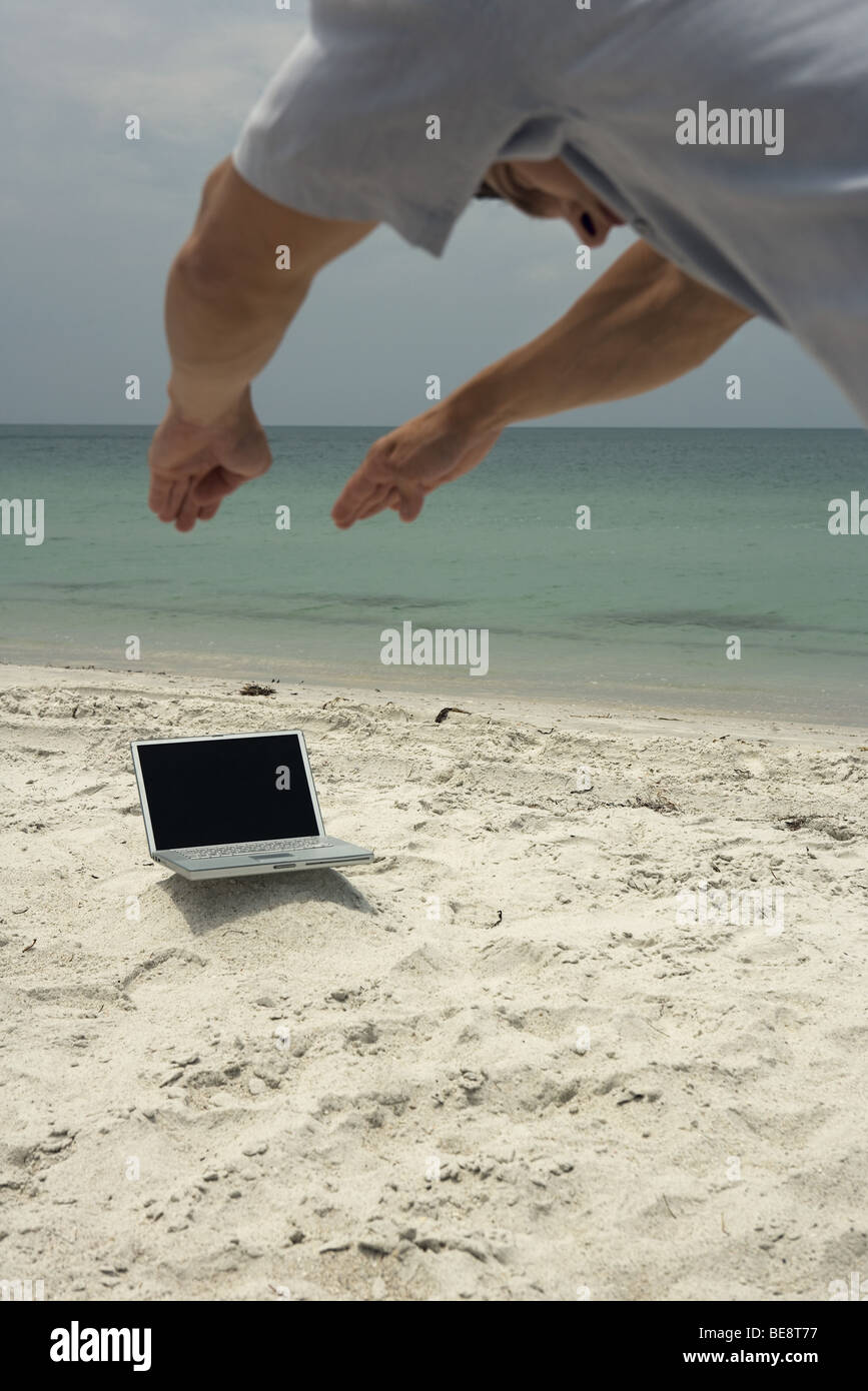 Mann am Strand, bücken, als ob Tauchen in Laptop-Computer, beschnitten Stockfoto
