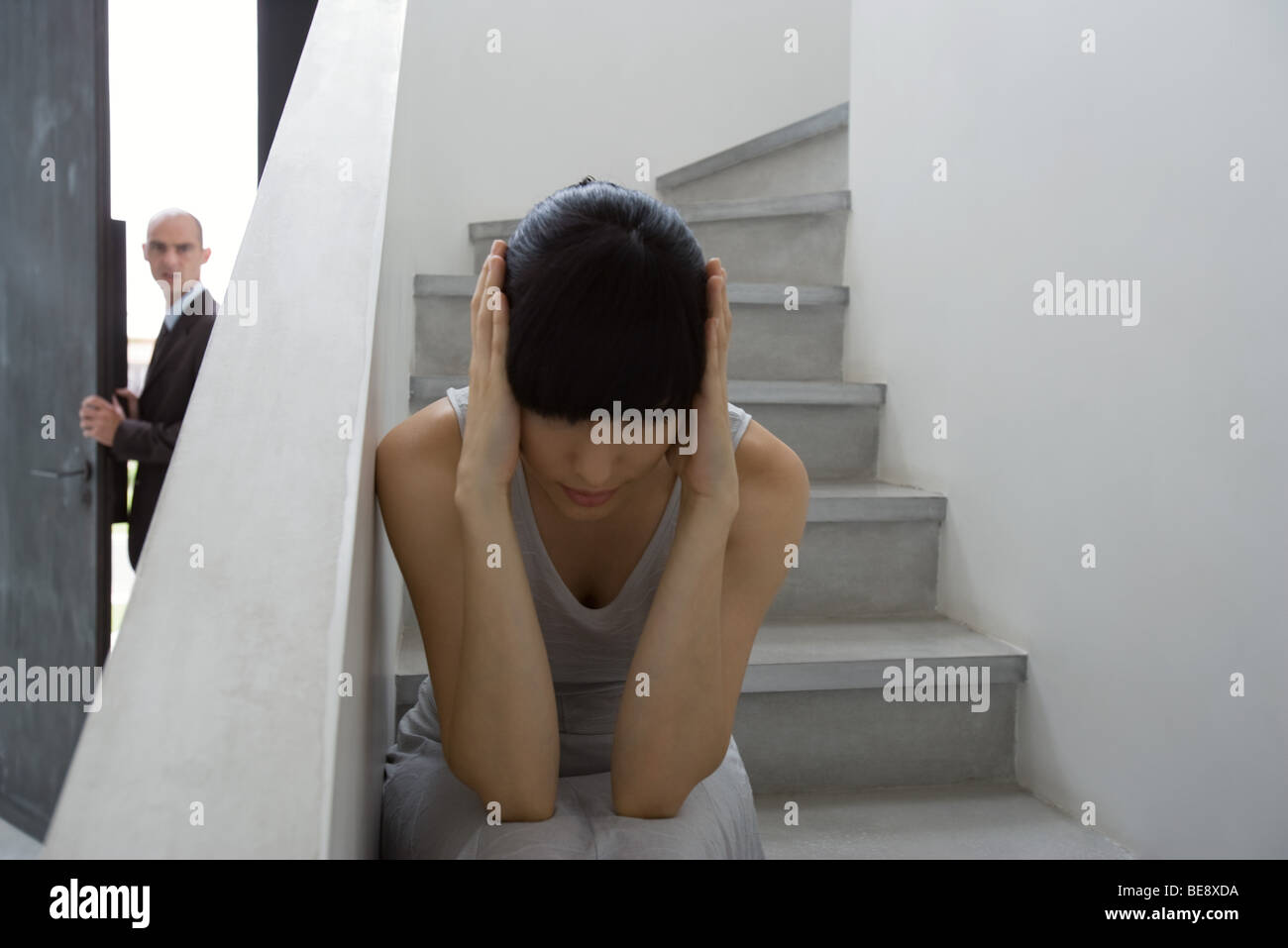 Frau sitzt auf der Treppe mit Händen über Ohren, Mann im Hintergrund Stockfoto