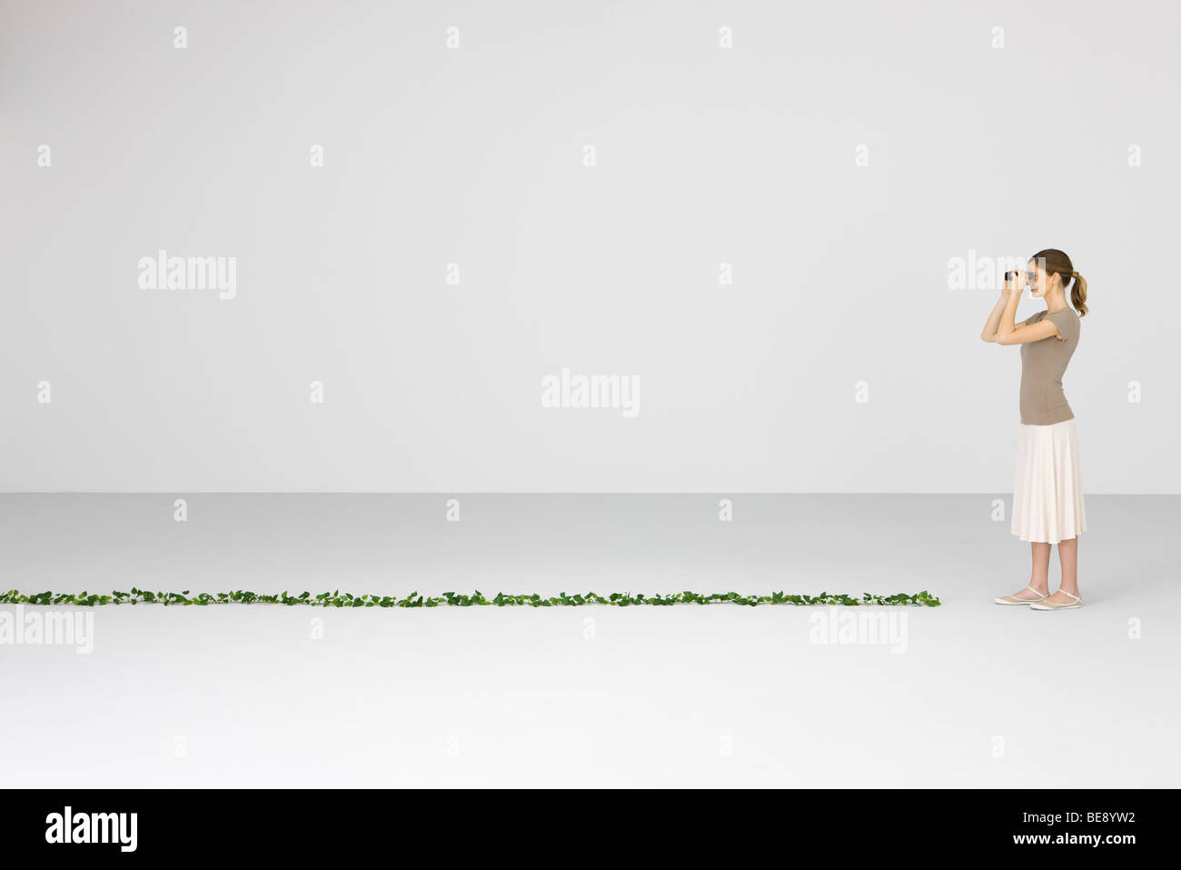 Frau, die durch ein Fernglas, lange Rebe auf Boden vor ihr Stockfoto