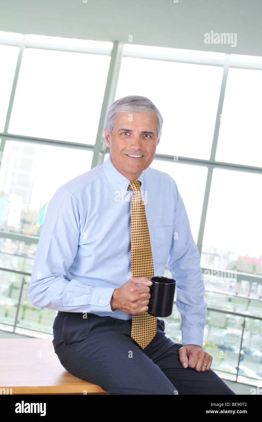 Geschäftsmann, sitzen auf Ecke seines Schreibtisches mit Kaffee-Haferl Stockfoto