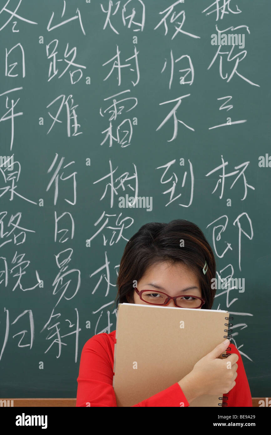 Student, versteckt sich hinter Notizblock vor chinesischen Schriftzeichen geschrieben an Tafel Stockfoto