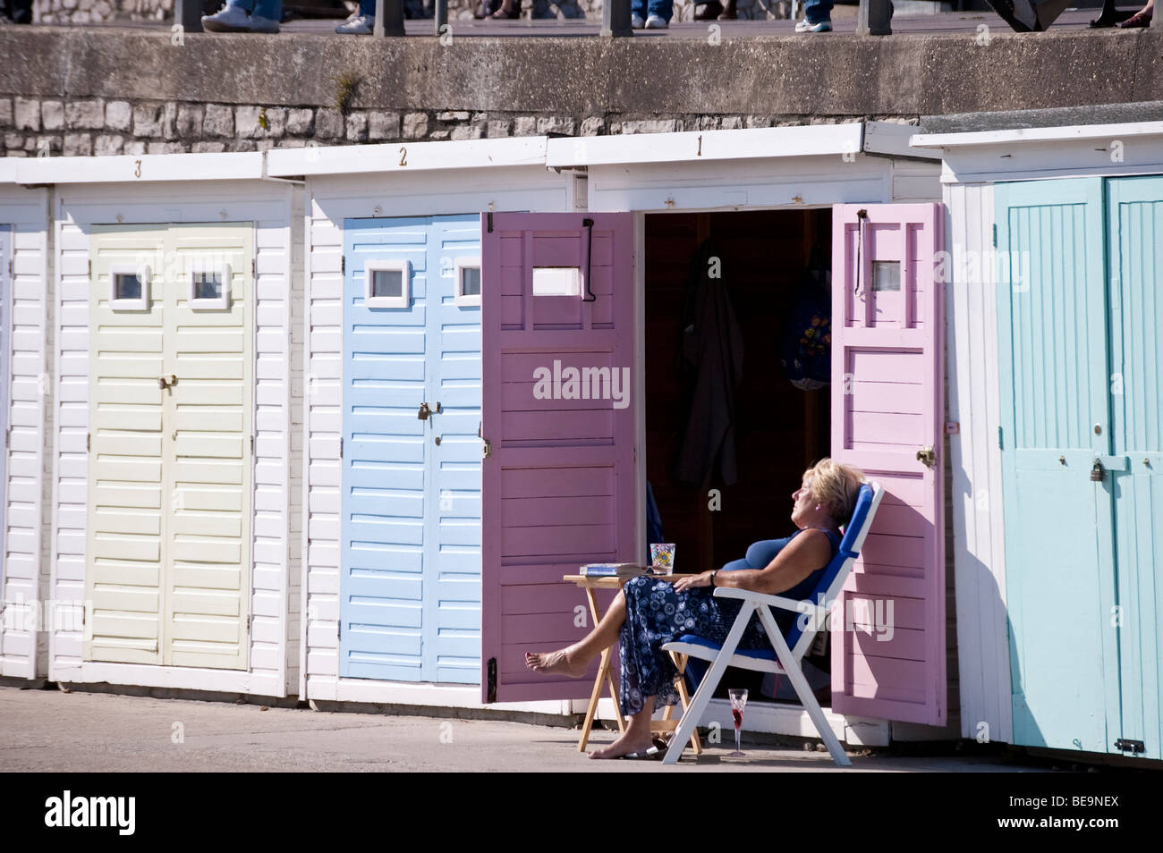 Frauen im mittleren Alter Sonnenbaden am Liegestuhl von Open Doors der Strandhütte mit Buch und ein Glas Wein Stockfoto