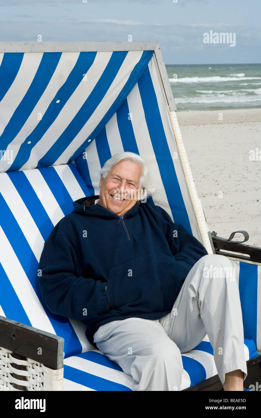 Ein senior Mann sitzend auf einem Strandstuhl mit Kapuze Stockfoto