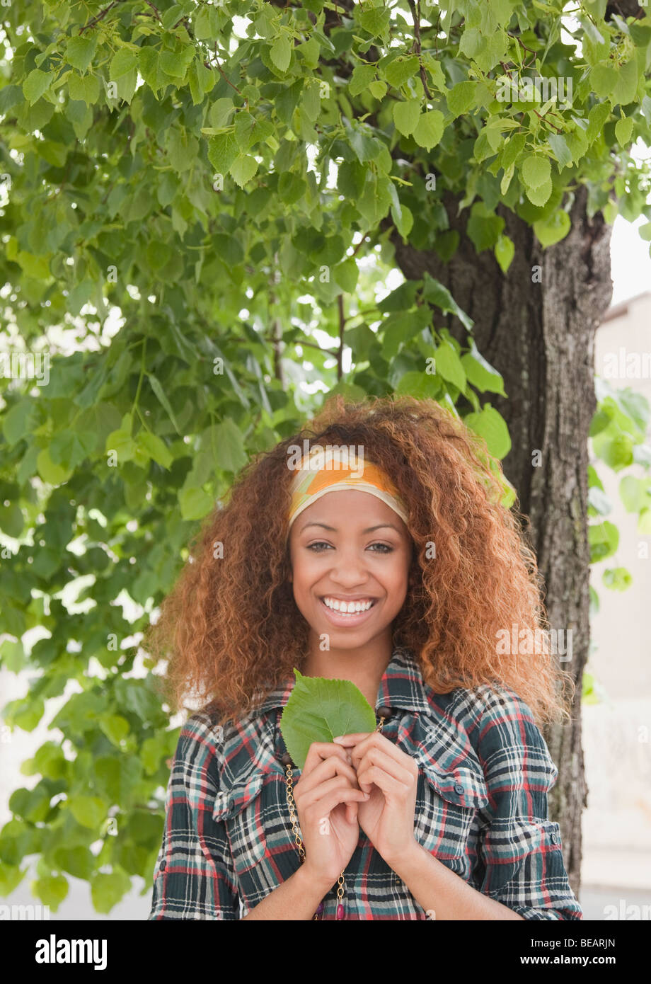 Gemischte Rassen Frau hält Blatt unter Baum Stockfoto