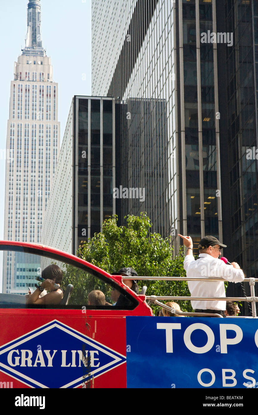 New York. Ein Reiseleiter steht auf einem Gray Line Bus und verweist auf das Empire State building (im Hintergrund) Stockfoto