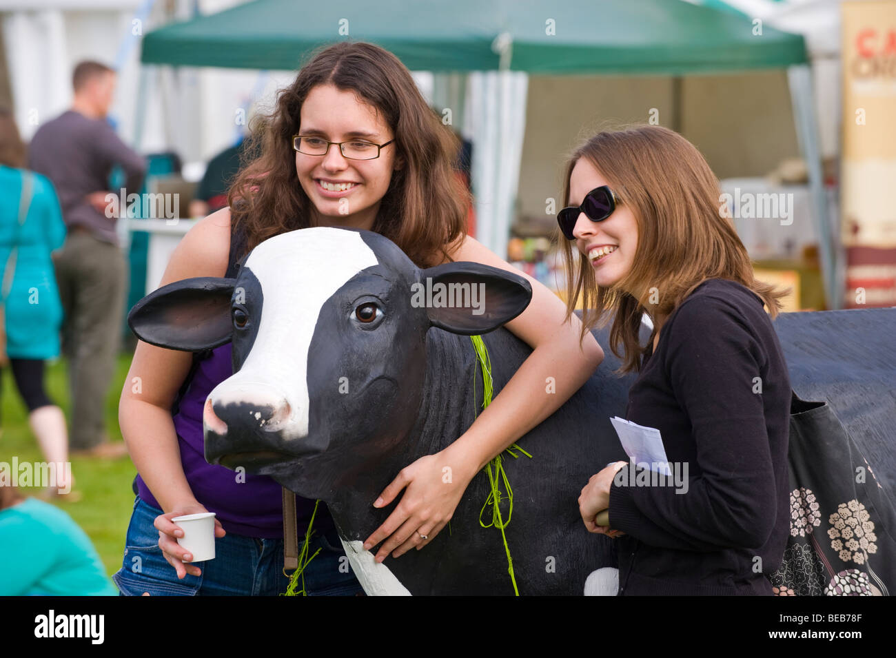 Zwei junge Frauen haben ihr Foto mit Werbe Kunststoff Kuh an der großen britischen Käse Festival Cardiff South Wales UK Stockfoto
