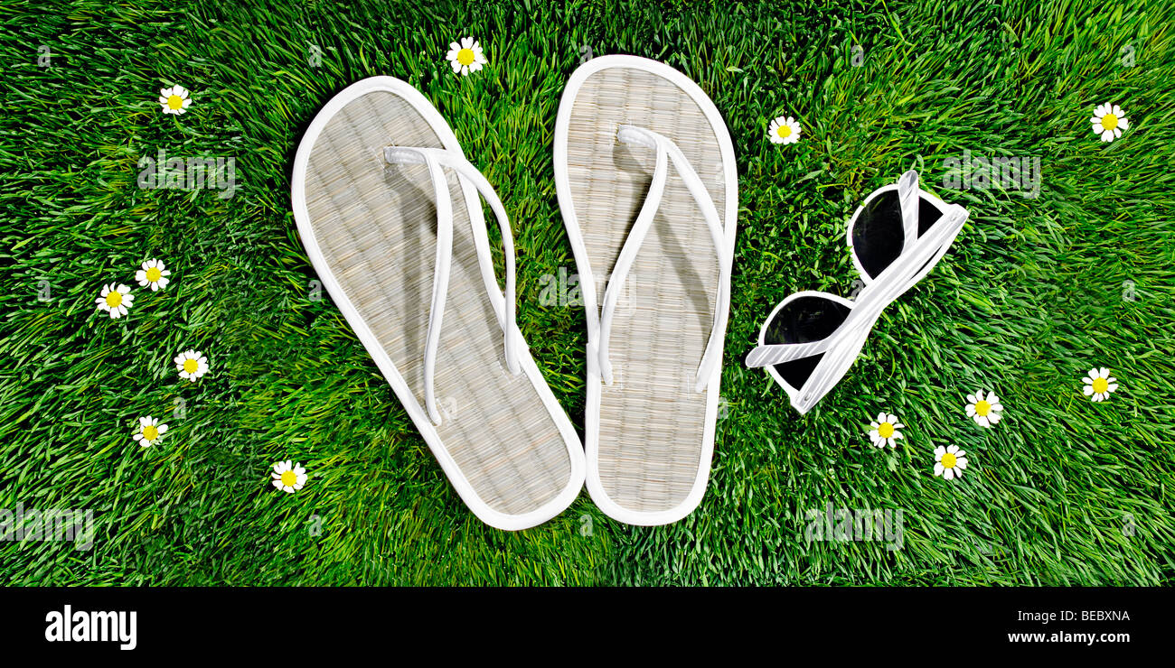 Sandalen und Sonnenbrillen auf einem Bett aus Rasen und Blumen, Frühling, Sommer und Entspannung zu veranschaulichen. Stockfoto