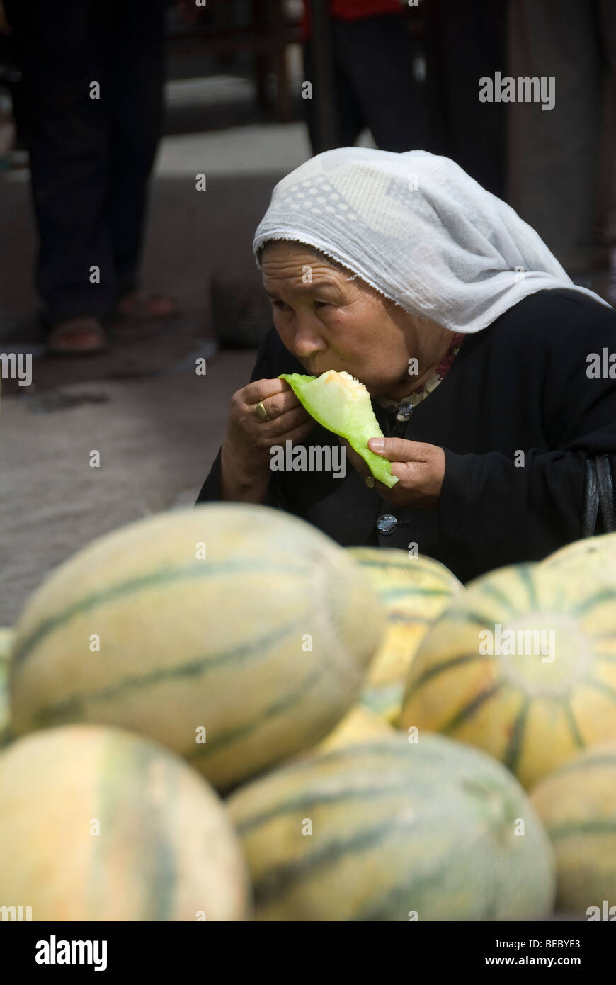 Muslimische Frau Essen Melone in einem Markt von Kashgar, Provinz Xinjiang, China. Stockfoto