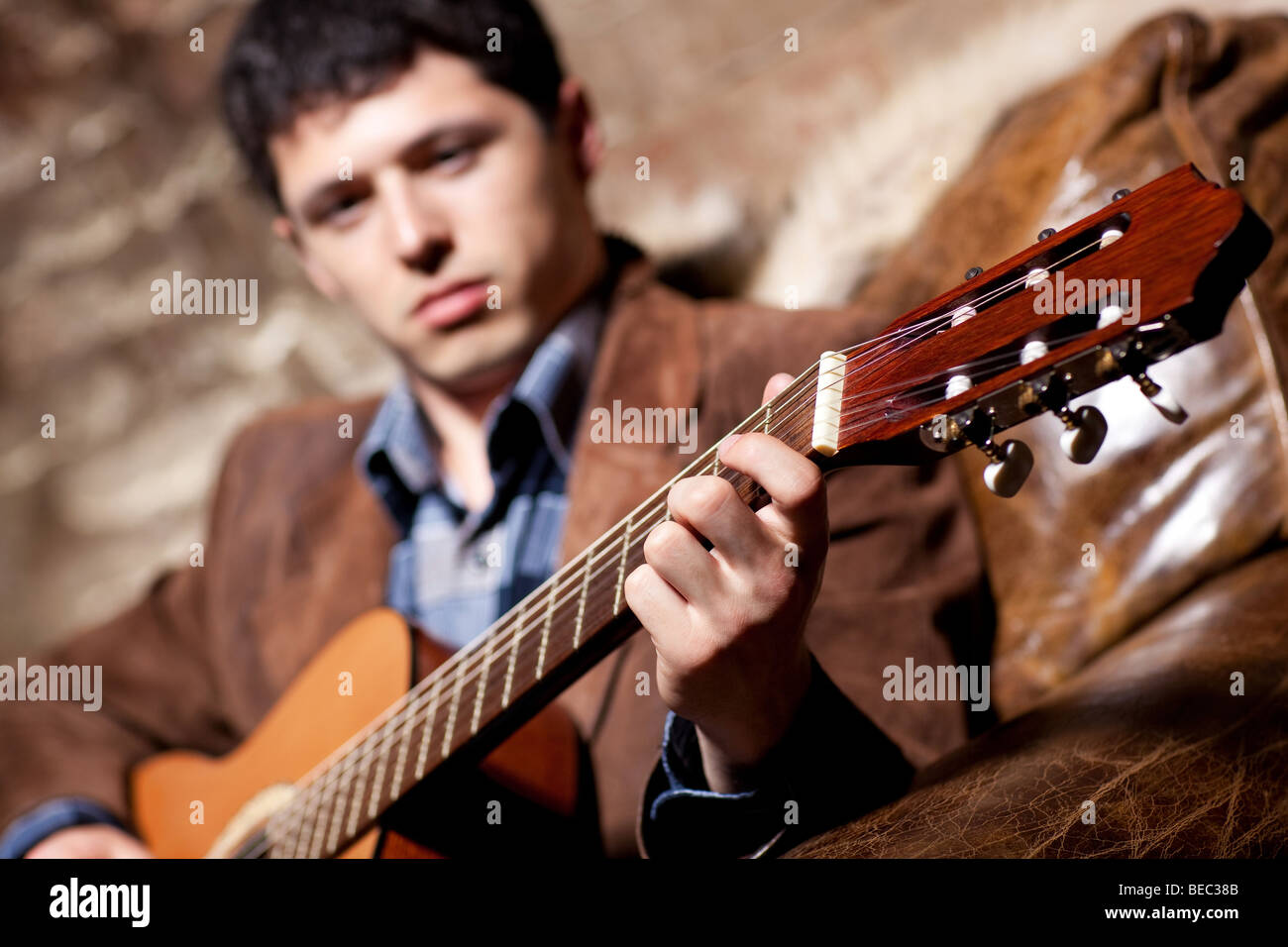 Junger Mann an der Gitarre in einem Sessel sitzend spielen. Auf Seite konzentrieren. Stockfoto