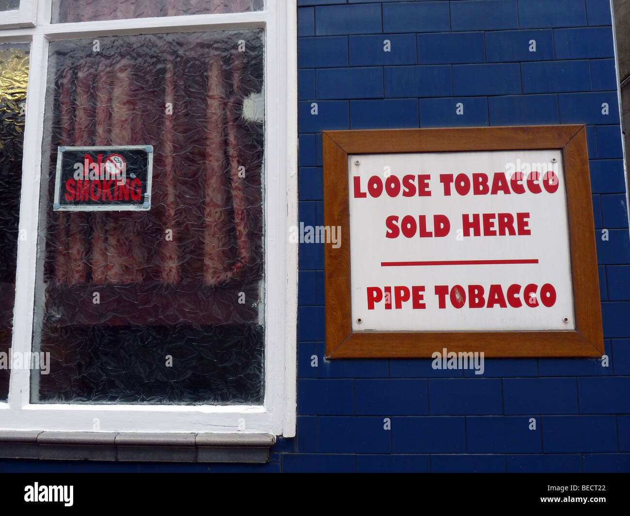 Weißes Schild Fett "lose Tabak verkauft hier" auf einer blauen gefliesten Wand mit einem "Rauchen verboten" Schild in einem nahe gelegenen Fenster Stockfoto