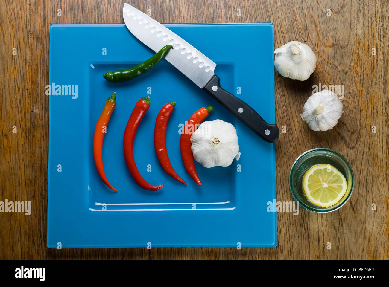 Frische rote und grüne Peperonccini, japanische Messer, blaue Platte Stockfoto