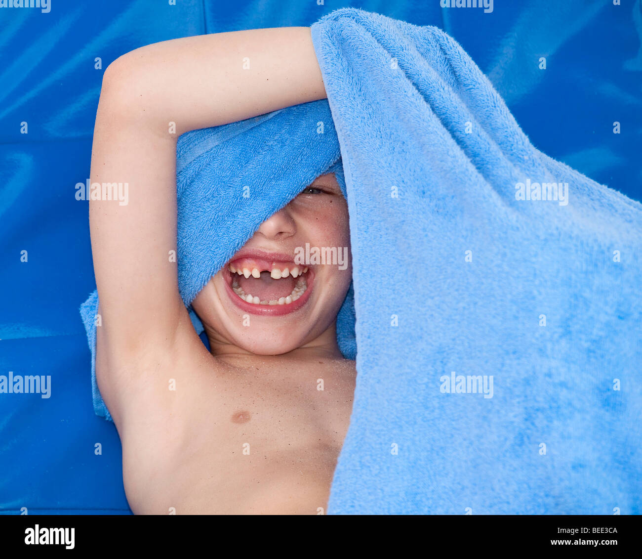 6-jähriger Junge mit einer Zahnlücke versteckt sich hinter einem Schwimmsachen lachen Stockfoto