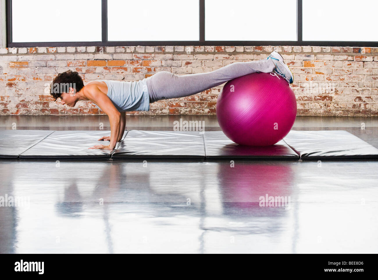 Eine junge Frau, die in einem Fitnessclub auf einer Matte aufpushups macht, während sie ihre Beine/Füße auf einem Trainingsball ausgleicht. Stockfoto
