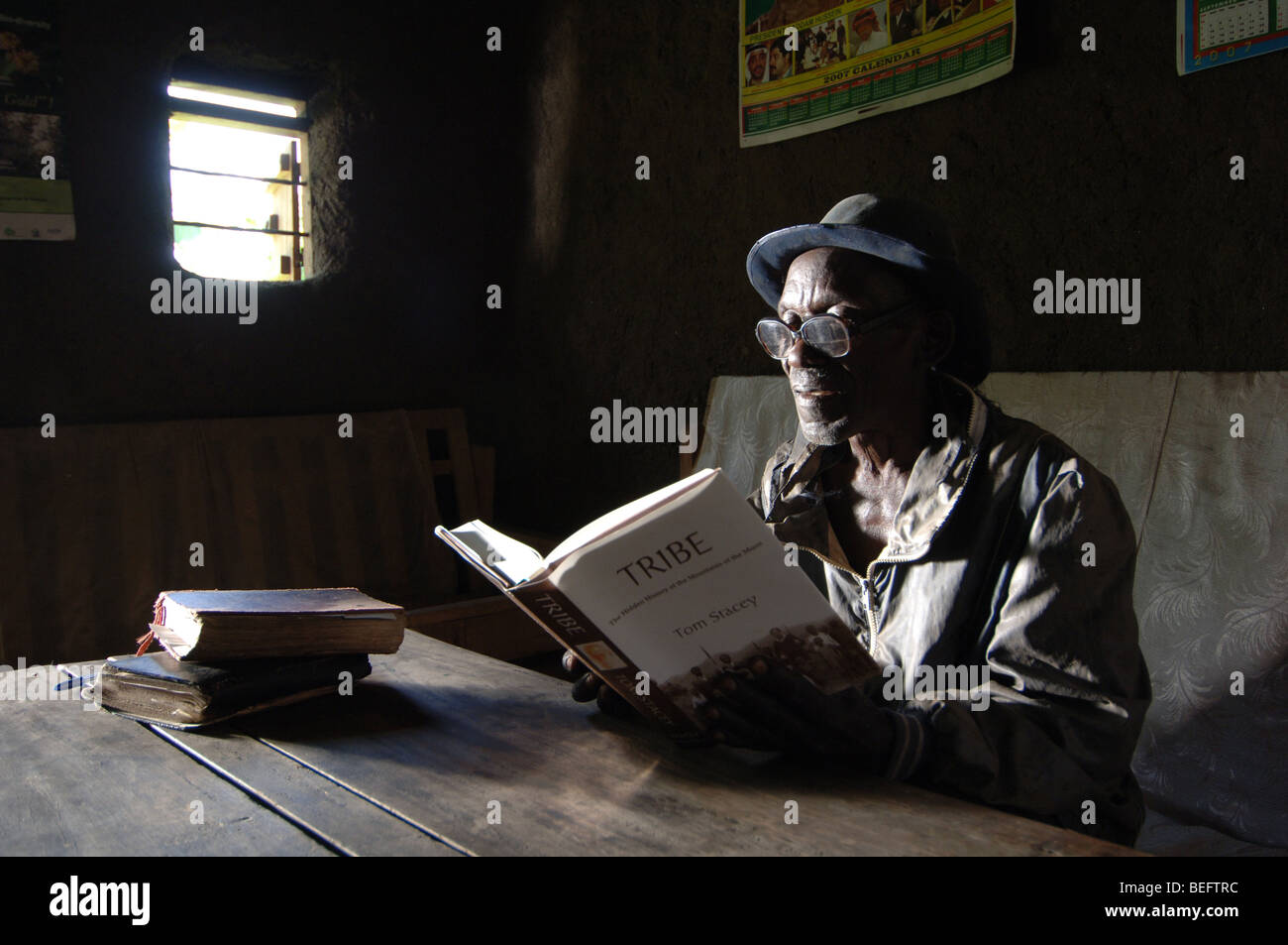Bakonzo Mann liest im Wohnzimmer von Mudhut, Ruwenzori-Gebirge, West-Uganda, Afrika, Plakat Kizza Besigye Führer opposition Stockfoto