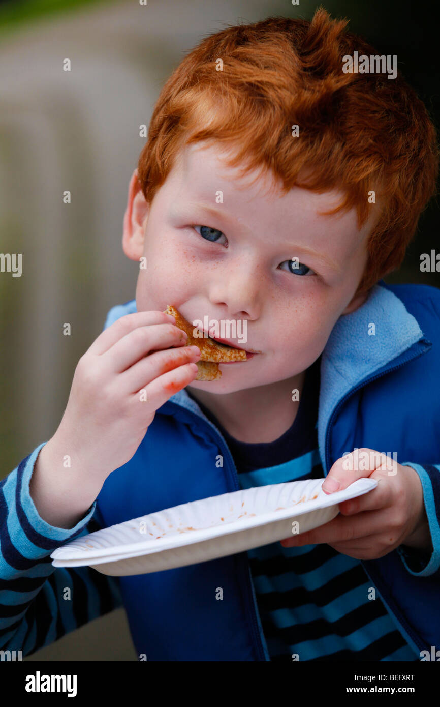 Fünf Jahre alter Junge mit roten Haaren einen Pfannkuchen auf der Straße Essen Stockfoto