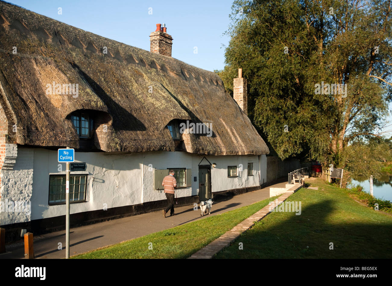 England, Cambridgeshire, Hemingford Grey, Mann, Hund vorbei an idyllischen Reetdachhaus am Flussufer Stockfoto