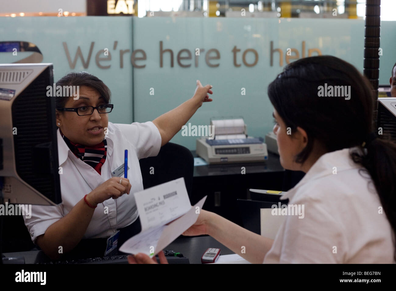 Ein weibliches Mitglied des Personals gibt Anweisungen an der British Airways-Information in der Abflughalle am Flughafen Heathrow Terminal 5 Stockfoto