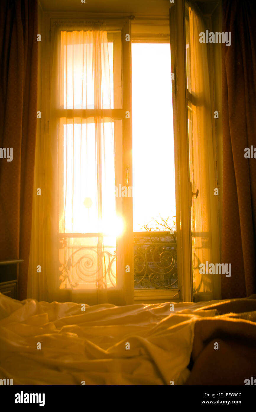 Sonnenaufgang, das durch die Fensterläden eines Hotelzimmers Parisain, beleuchten die ungemachten Bett Stockfoto