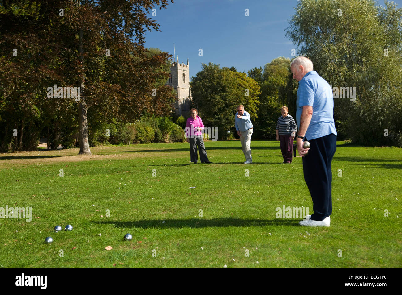 England, Cambridgeshire, Huntingdon, Hartford, Rentner spielen Boule am Flussufer grün unter Kirchturm Stockfoto