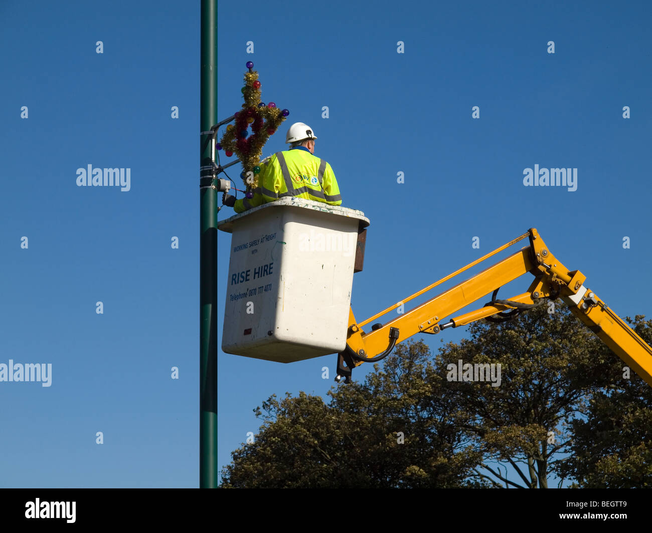 Lokale Behörde Arbeiter Befestigung Weihnachtsbeleuchtung an einem Lampost Anfang Oktober Stockfoto