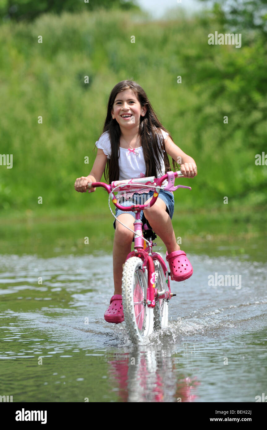 Fröhliches junges Mädchen Reiten Fahrrad über flachem Wasser Stockfoto