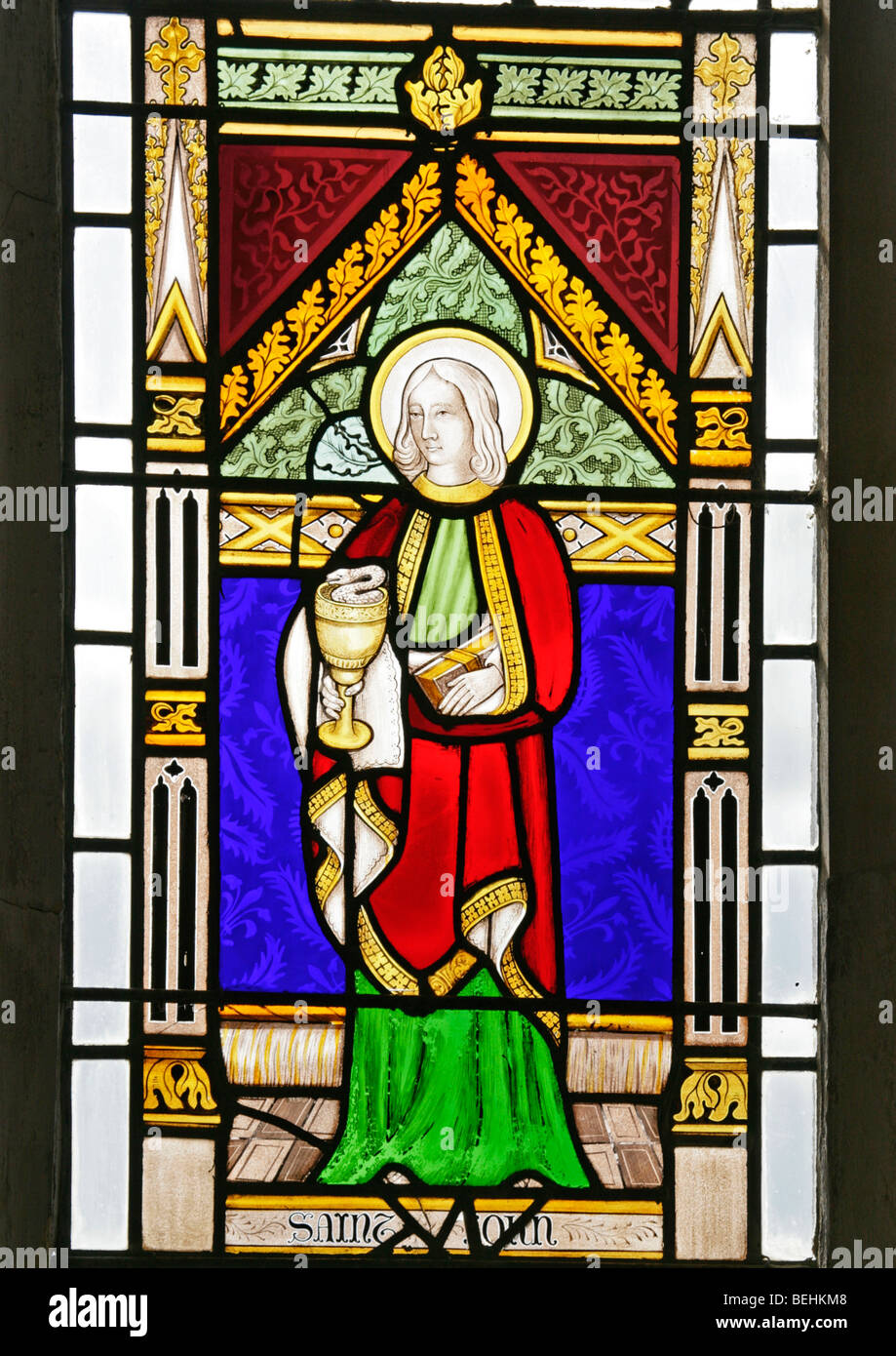 Ein Glasfenster von Joseph Grant von Costessey, das den heiligen Johannes des Apostels darstellt und einen Kelch aus Schlange, Allerheiligenkirche, Wighton, Norfolk, hält Stockfoto