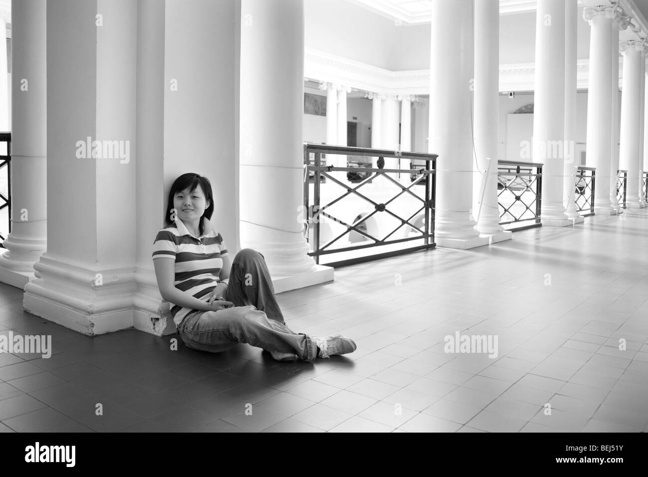 Junge Chinesin sitzt in einem sehr großen oberen Balkon mit Spalten. Stockfoto